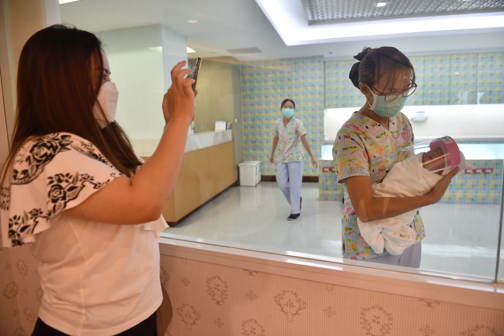 A mother takes a photo of her newborn baby who is wearing a face shield, in an effort to halt the spread of the COVID-19 coronavirus, at Praram 9 Hospital in Bangkok on April 9, 2020.