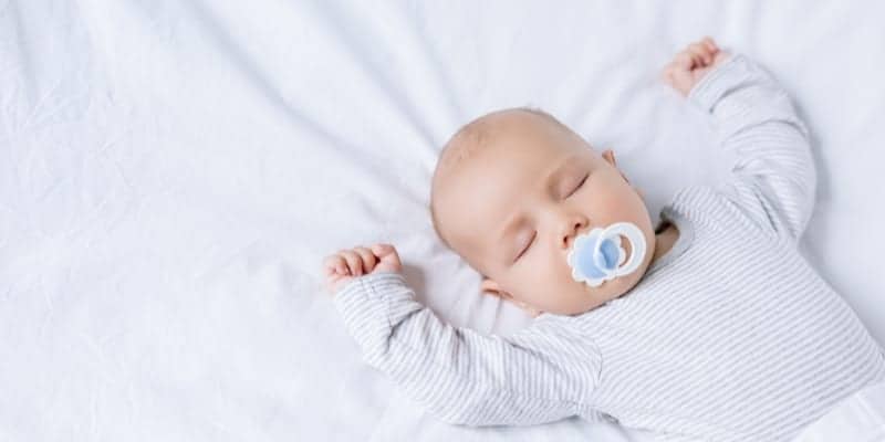 cluster feeding baby lying on bed with pacifier and arms up