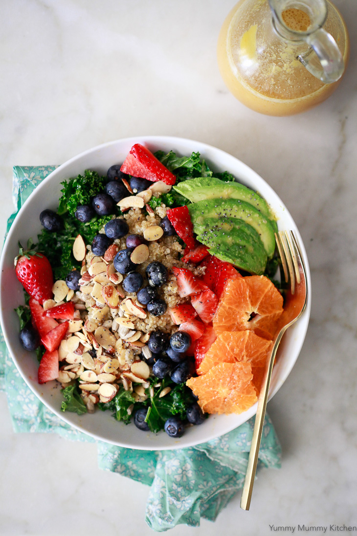 A delicious vegan kale superfood salad with blueberries, strawberries, quinoa, avocado, nuts, and seeds. This salad is served with orange vinaigrette. 