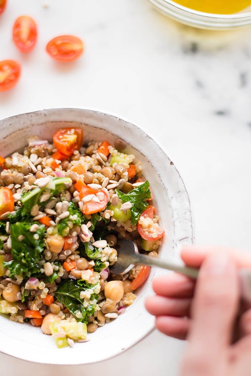 Serving bowl of quinoa lentil salad with lemon vinaigrette dressing, ready to be enjoyed by a hand with a fork, taking a bite.
